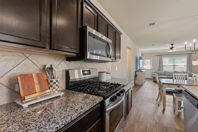 Kitchen with stainless steel appliances, stone counters, open floor plan, light wood finished floors, and backsplash | Image 9