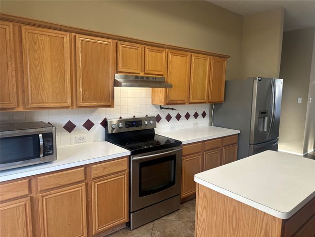 Kitchen featuring under cabinet range hood, stainless steel appliances, decorative backsplash, and light countertops | Image 10