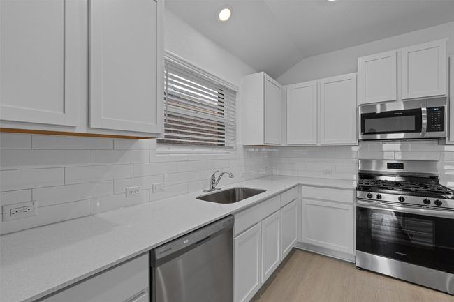 Kitchen featuring stainless steel appliances, lofted ceiling, white cabinetry, light wood-style floors, and decorative backsplash | Image 6