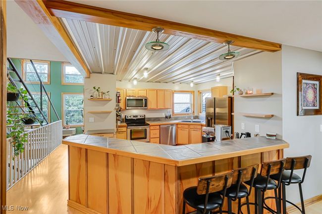 Kitchen with tile countertops, appliances with stainless steel finishes, a peninsula, open shelves, and beam ceiling | Image 20