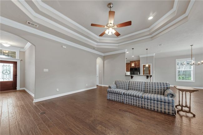 Living area with arched walkways, a raised ceiling, dark wood-style floors, crown molding, and ceiling fan | Image 8