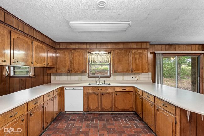 Kitchen featuring white dishwasher, a sink, a peninsula, brown cabinetry, and wooden walls | Image 13