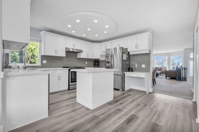 Kitchen with under cabinet range hood, a sink, tasteful backsplash, stainless steel appliances, and light wood finished floors | Image 10