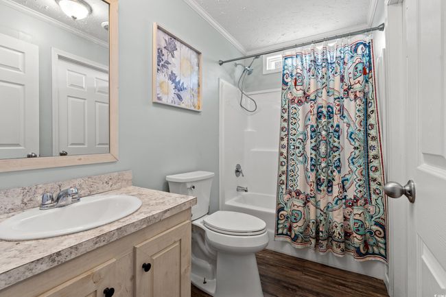 Full bathroom featuring crown molding, vanity, shower / bathtub combination with curtain, wood finished floors, and a textured ceiling | Image 23