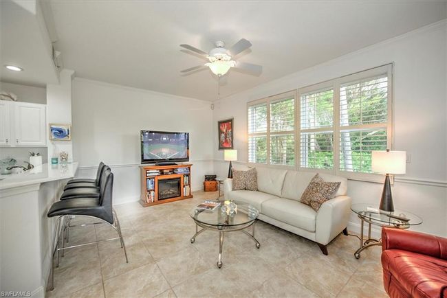 Living area with crown molding, a glass covered fireplace, light tile patterned floors, baseboards, and ceiling fan | Image 6