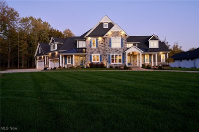 This image captures the elegant front exterior of the home at dusk. The stone facade, contrasted by dark siding and white trim, adds to the home’s stately appearance. | Image 2