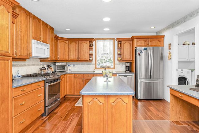 Kitchen with washer / clothes dryer, open shelves, appliances with stainless steel finishes, wood finished floors, and backsplash | Image 7