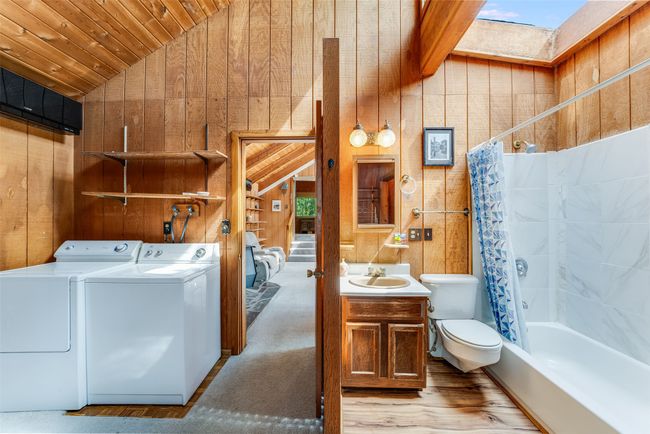 Full bath with washing machine and dryer, lofted ceiling, wood walls, vanity, and toilet | Image 27