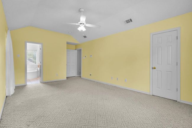 Unfurnished bedroom with light colored carpet, lofted ceiling, ensuite bathroom, and a ceiling fan | Image 14