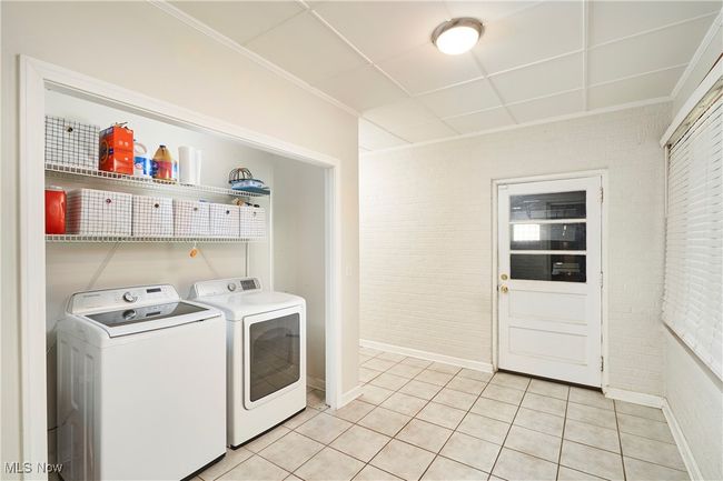 Clothes washing area featuring washer and clothes dryer, baseboards, light tile patterned floors, and brick wall | Image 16