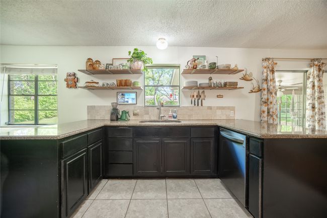 Kitchen with stainless steel dishwasher, open shelves, a sink, a peninsula, and light tile patterned flooring | Image 9
