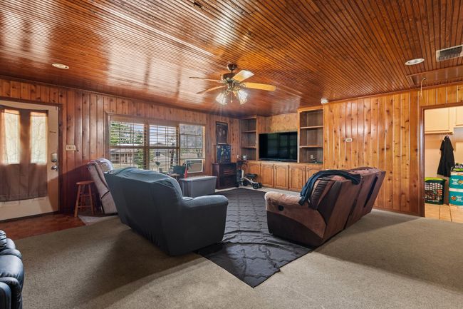 Carpeted living room with wooden walls, visible vents, and ceiling fan | Image 27