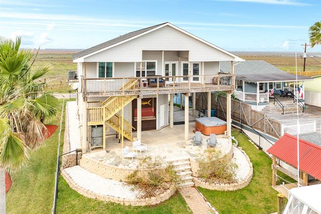 56 Marlin an elevated coastal home with a spacious deck and staircase access. Features a large patio area with seating, a hot tub, and landscaped surroundings. Ideal for enjoying outdoor and canal front living and scenic views. | Image 22