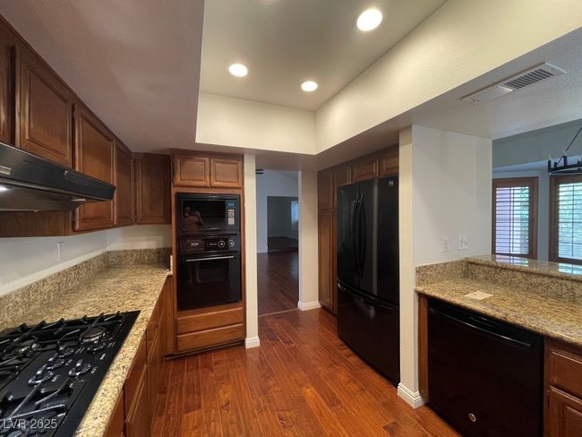 Kitchen featuring black appliances, ventilation hood, dark wood-type flooring, light countertops, and recessed lighting | Image 6