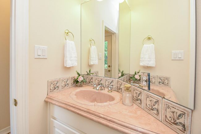 This bathroom features a pink marble countertop with decorative tile accents. It includes a large mirror, gold fixtures, and towel rings, creating a classic and elegant feel. | Image 38
