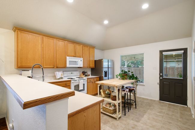 Kitchen featuring white appliances, lofted ceiling, light countertops, a peninsula, and recessed lighting | Image 8