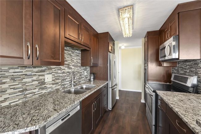 Kitchen featuring backsplash, dark wood-type flooring, light stone counters, stainless steel appliances, and a sink | Image 15