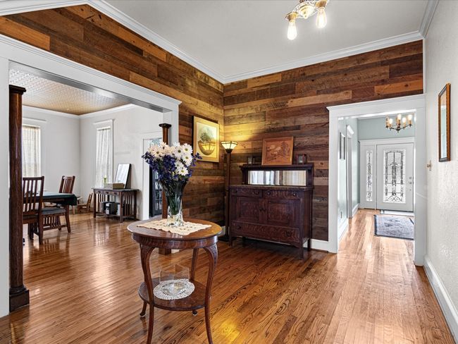 Entrance foyer and standing area with wood finished floors, baseboards, an inviting chandelier, wood walls, and crown molding | Image 6