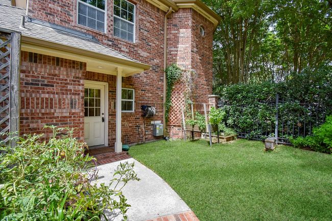 Charming backyard with a brick exterior, featuring a small covered patio area, lush grass, and a garden space. Ideal for outdoor relaxation and gardening. | Image 46