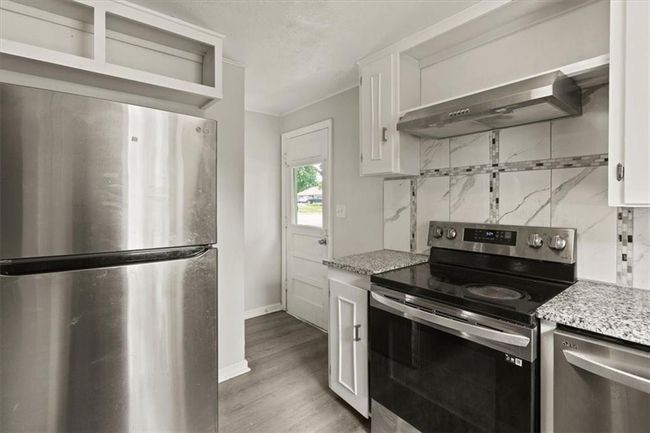 Kitchen with stainless steel appliances, range hood, decorative backsplash, and white cabinetry | Image 13