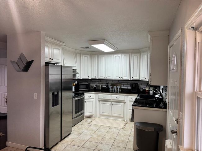 Kitchen featuring sink, light tile patterned floors, backsplash, stainless steel appliances, and white cabinets | Image 6