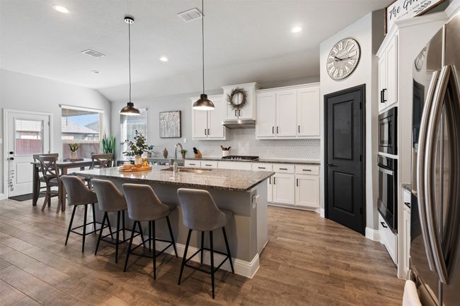 Kitchen featuring stainless steel appliances, visible vents, dark wood-type flooring, a sink, and a kitchen bar | Image 12