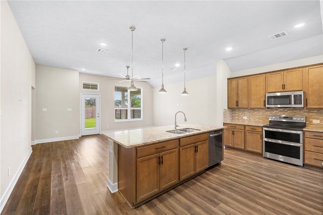 Kitchen with stainless steel appliances, a sink, brown cabinets, dark wood finished floors, and tasteful backsplash | Image 15