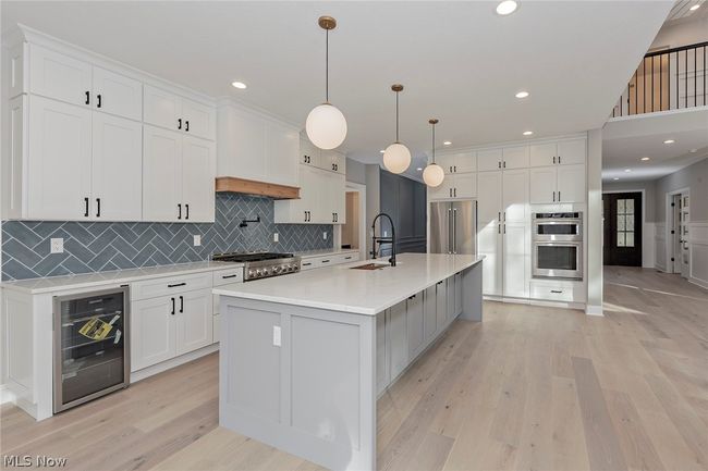 Kitchen featuring light hardwood / wood-style floors, appliances with stainless steel finishes, a kitchen island with sink, beverage cooler, and tasteful backsplash | Image 23