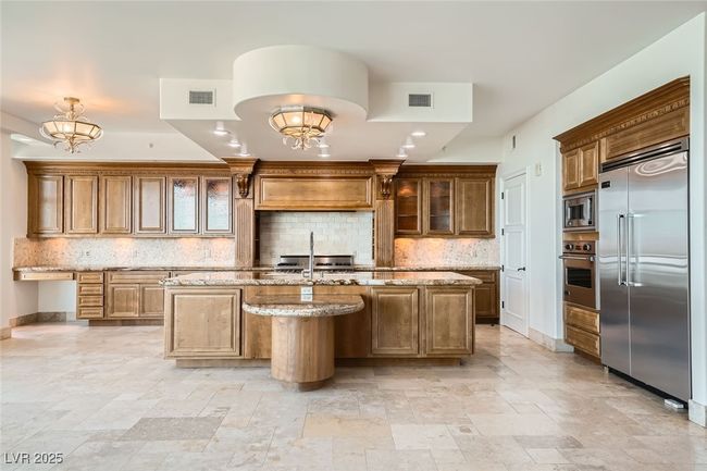 Kitchen with built in appliances, an island with sink, stone tile flooring, and tasteful backsplash | Image 15