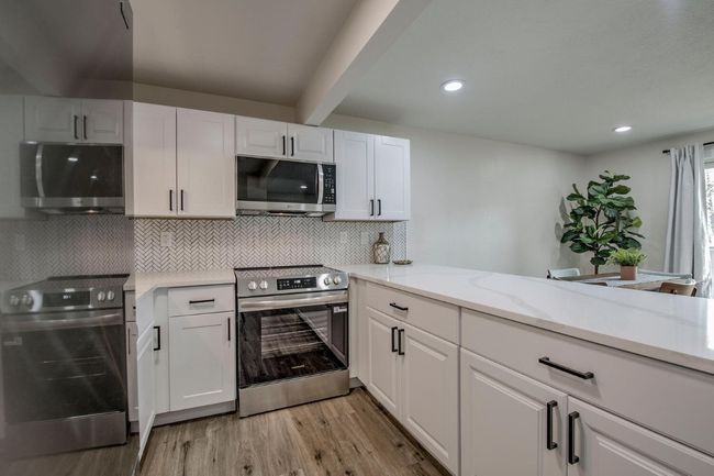Kitchen with light wood finished floors, light stone countertops, stainless steel appliances, tasteful backsplash, and white cabinets | Image 13