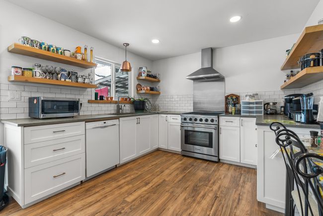 Kitchen with open shelves, a sink, appliances with stainless steel finishes, dark countertops, and wall chimney range hood | Image 15