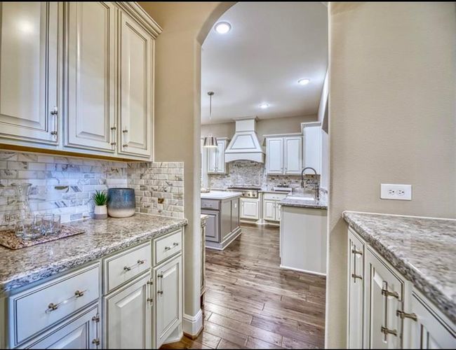 This photo showcases a modern kitchen with elegant white cabinetry, granite countertops, and a stylish tile backsplash. The space features stainless steel appliances and recessed lighting, creating a bright and inviting atmosphere. The hardwood flooring adds warmth to the room, enhancing its overall appeal. | Image 16