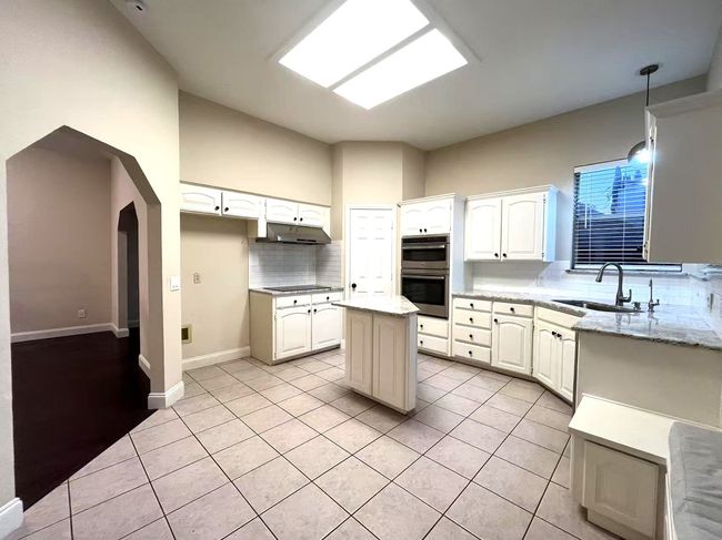 Kitchen featuring under cabinet range hood, double oven, backsplash, light tile patterned flooring, and arched walkways | Image 11