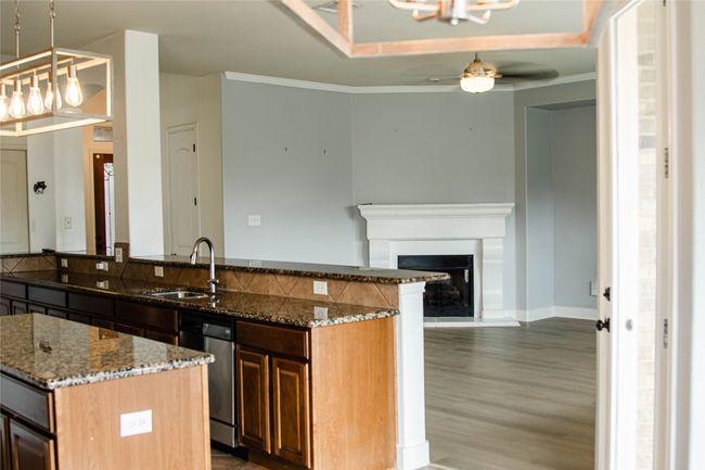 Kitchen with dishwasher, ceiling fan, wood finished floors, a kitchen island, and stone counters | Image 9