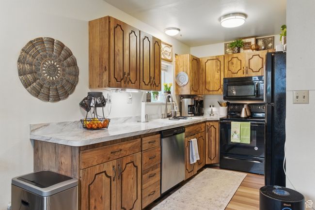Kitchen with a sink, light wood-style floors, brown cabinetry, light countertops, and black appliances | Image 39