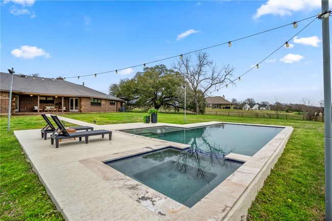 View of swimming pool featuring a pool with connected hot tub, a patio area, a yard, and fence | Image 47