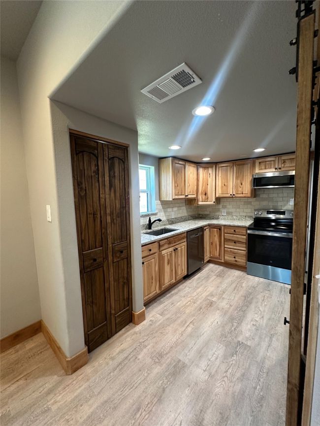 Kitchen featuring light wood-style flooring, exhaust hood, stainless steel electric stove, visible vents, and black dishwasher | Image 12