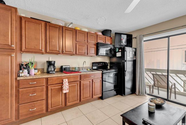 Kitchen with brown cabinetry, light tile patterned flooring, a sink, black appliances, and a textured ceiling | Image 24