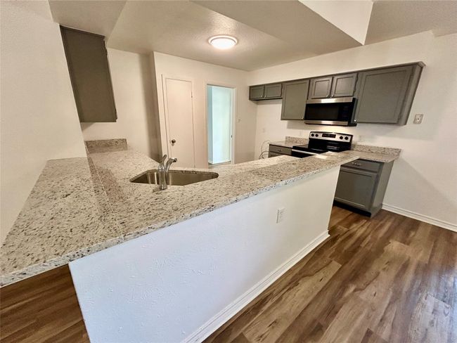 Kitchen featuring stainless steel appliances, a sink, light stone counters, a peninsula, and dark wood-style flooring | Image 8