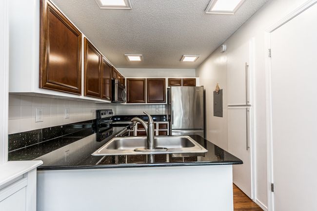 Kitchen featuring stainless steel appliances, a peninsula, a sink, dark brown cabinets, and backsplash | Image 5