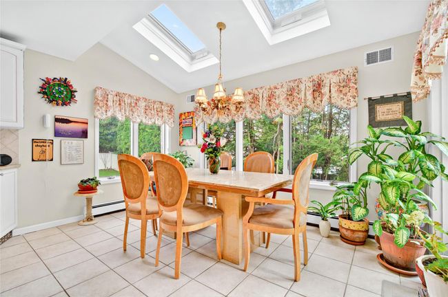 Dining area with a skylight, lofted ceiling, a chandelier, light tile patterned floors, and a baseboard heating unit | Image 22