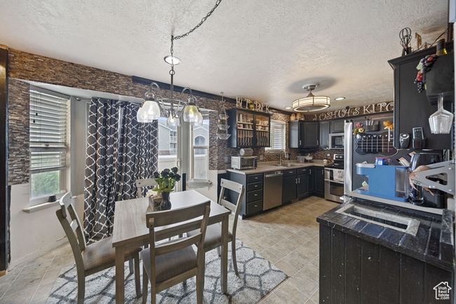 Kitchen with a textured ceiling, stainless steel appliances, a sink, light countertops, and an inviting chandelier | Image 6
