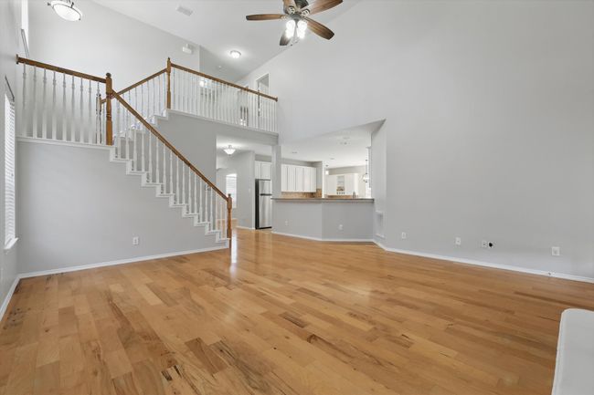 Unfurnished living room featuring ceiling fan, light wood-style floors, stairs, baseboards, and a high ceiling | Image 8
