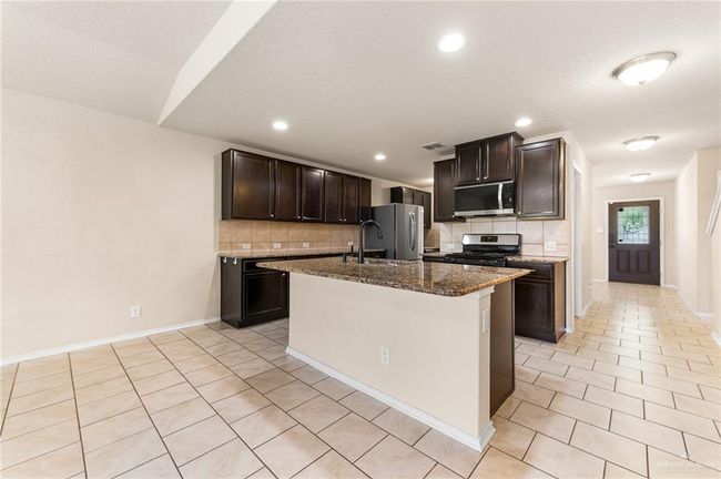 Kitchen with stainless steel appliances, decorative backsplash, light tile patterned floors, dark stone countertops, and recessed lighting | Image 7