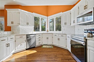 Kitchen with dark hardwood tyle floors, white cabinetry, appliances with stainless steel finishes, and tasteful backsplash | Image 2