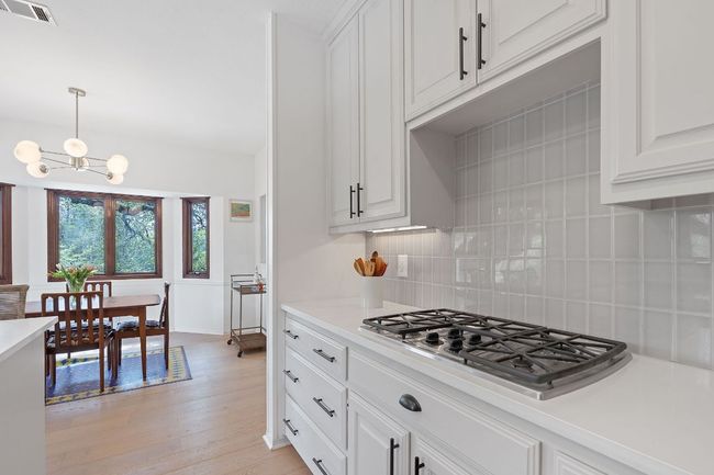 Kitchen with stainless steel gas stovetop, decorative backsplash, light wood-style flooring, light countertops, and a chandelier | Image 15