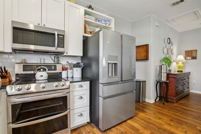 Kitchen featuring appliances with stainless steel finishes, visible vents, Corian countertops, and backsplash | Image 12