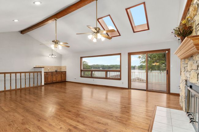 Unfurnished living room featuring light wood finished floors, a ceiling fan, a stone fireplace, and a wealth of natural light | Image 15
