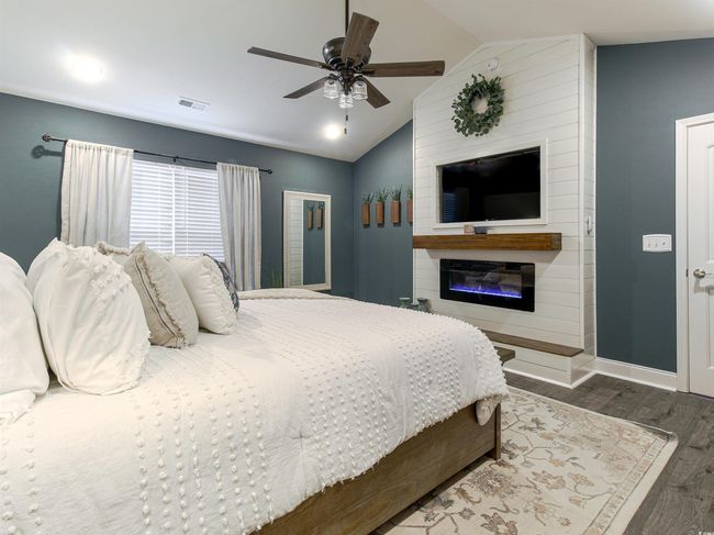 Bedroom featuring ceiling fan, dark wood-type flooring, a fireplace, and lofted ceiling | Image 19