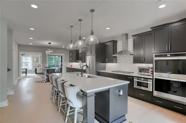A dramatic waterfall island anchors this designer kitchen, where contrasting cabinetry, sparkling pendant lights, and expansive custom pantry built-ins meet seamless flow to the dining area, covered deck | Image 10
